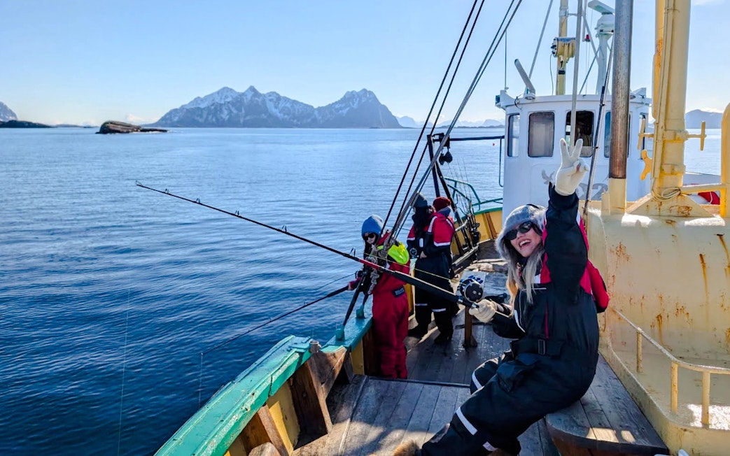 Woman fishing on a boat cruise in Lofoten with snowy mountains in the background.