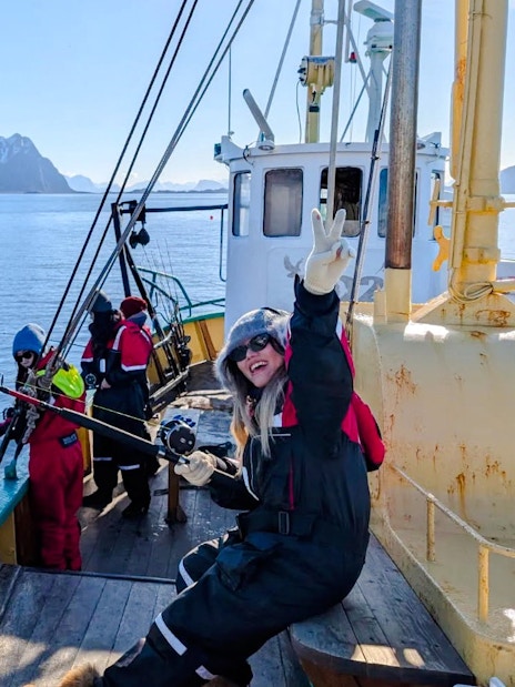 Woman fishing on a boat cruise in Lofoten with snowy mountains in the background.