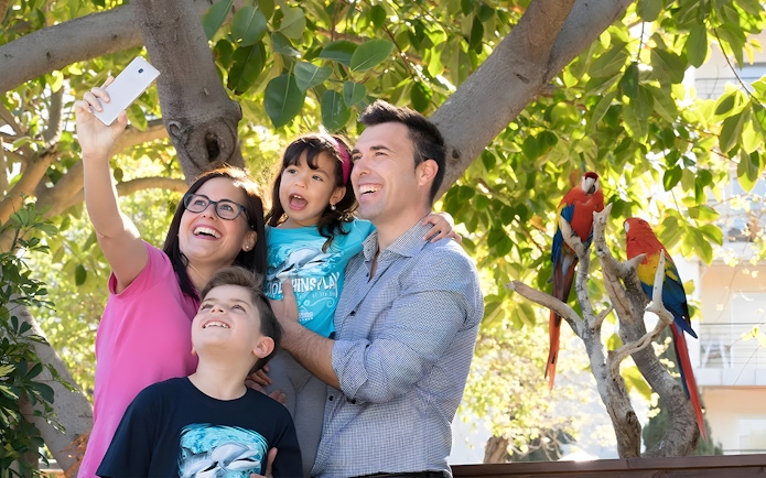Family taking selfie near colorful parrots at Marineland Mallorca aviary.
