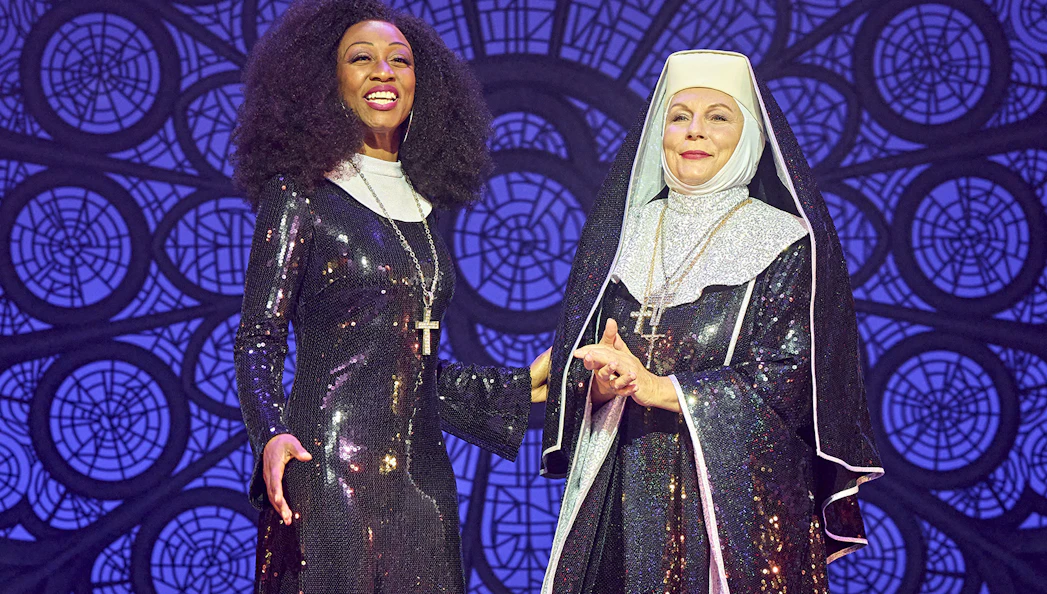 Two performers in sequined costumes from the musical Sister Act on stage.