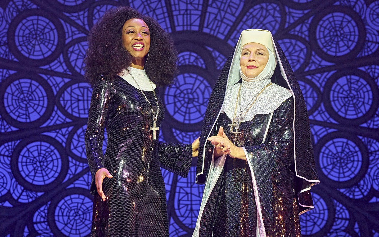 Two performers in sequined costumes from the musical Sister Act on stage.