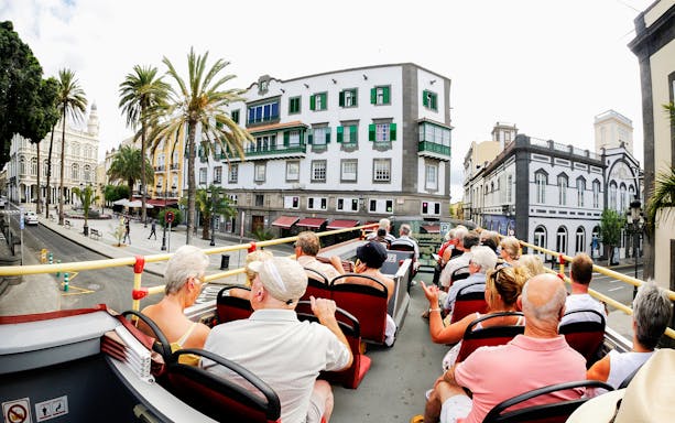 Tourists on a red double-decker bus in Las Palmas, viewing historic buildings.