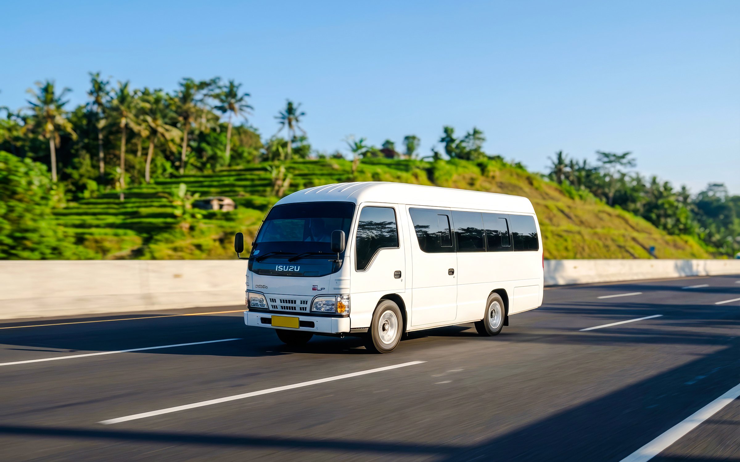 Elf Isuzu minibus driving on a highway with lush greenery in the background.