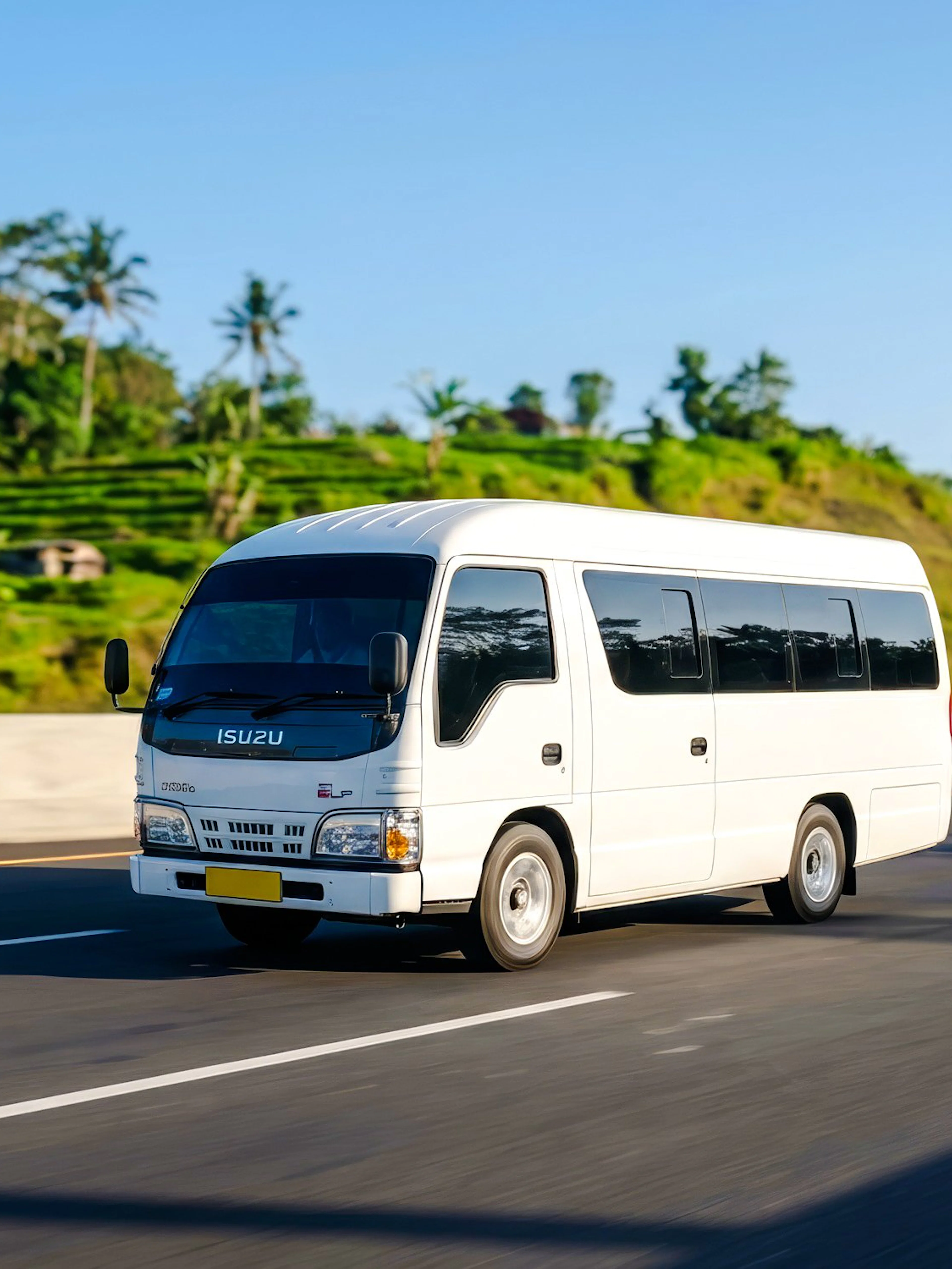 Elf Isuzu minibus driving on a highway with lush greenery in the background.