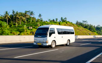Elf Isuzu minibus driving on a highway with lush greenery in the background.