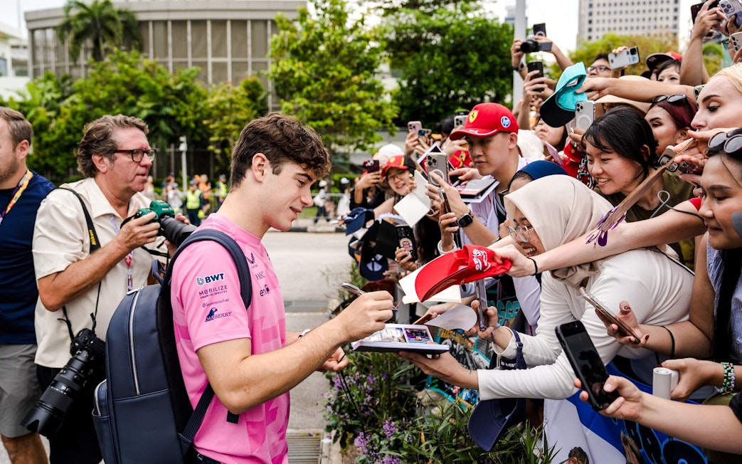 Race car driver signing autographs for fans at a public event.