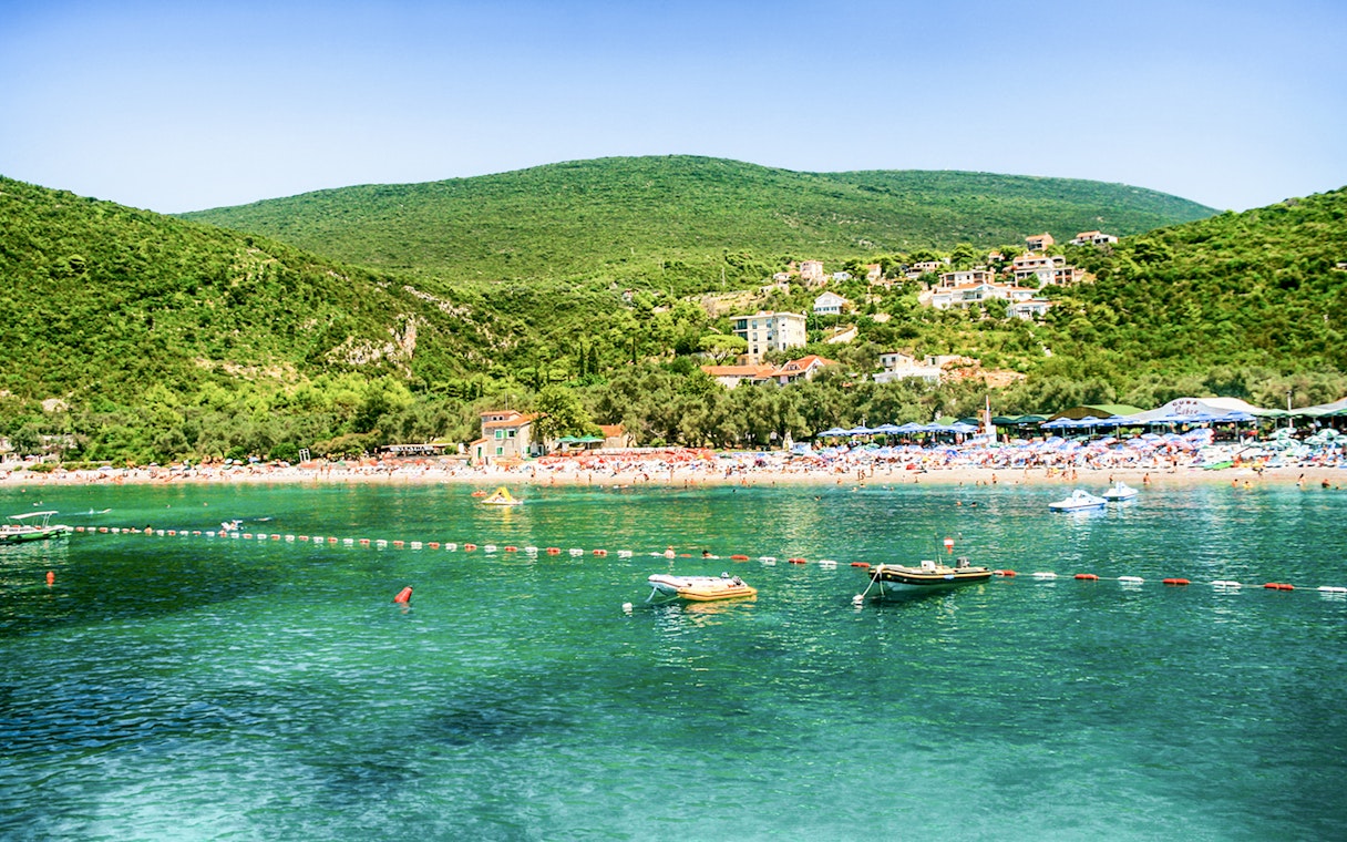 Zanjic Beach in Montenegro with boats and lush green hills in the background.
