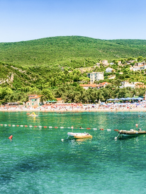 Zanjic Beach in Montenegro with boats and lush green hills in the background.