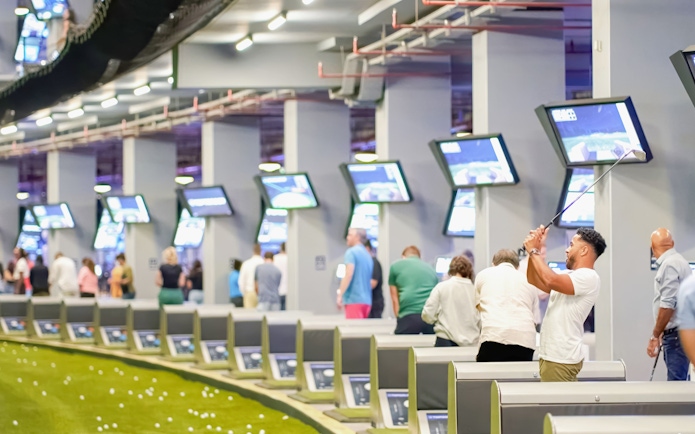 Golfers practicing at Topgolf Dubai with digital screens and driving range.