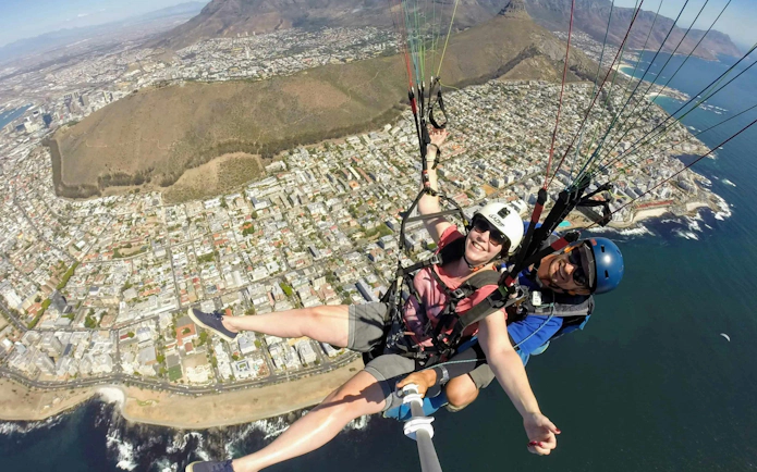 Tandem paragliding over Cape Town coastline with cityscape below.