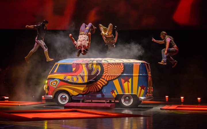 Performers doing acrobatics over a colorful van at The Beatles LOVE show.