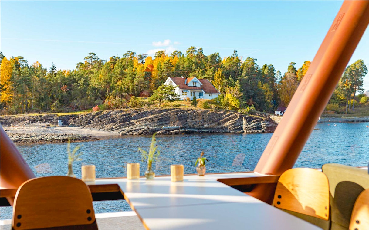 Silent fjord cruise view from Oslo with a house on a rocky shore and autumn trees.