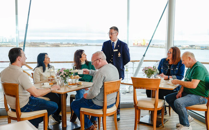 Guests enjoying afternoon tea on the Royal Yacht Britannia with a guide.