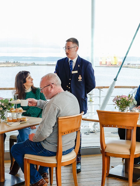 Guests enjoying afternoon tea on the Royal Yacht Britannia with a guide.