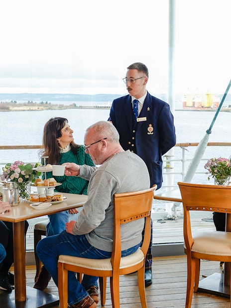 Guests enjoying afternoon tea on the Royal Yacht Britannia with a guide.
