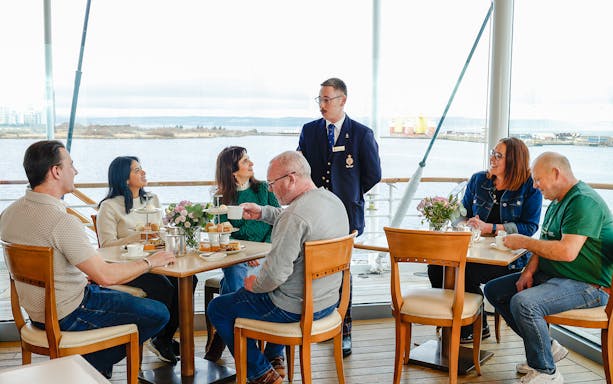 Guests enjoying afternoon tea on the Royal Yacht Britannia with a guide.