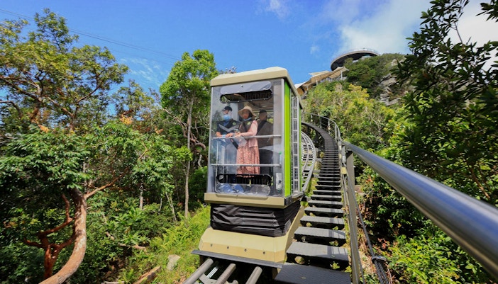 Tourist on SkyGlide cable car with panoramic view of Langkawi rainforest.