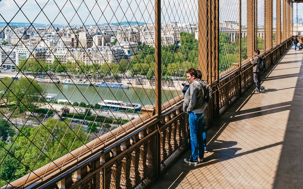 Visitors enjoying the view from the Eiffel Tower's second floor, overlooking the Seine River in Paris.
