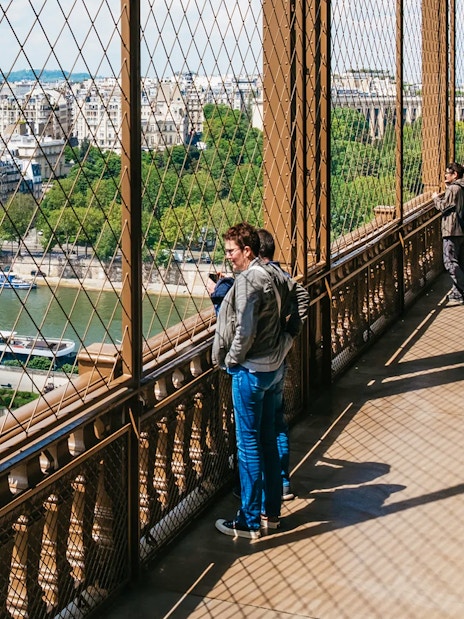 Visitors enjoying the view from the Eiffel Tower's second floor, overlooking the Seine River in Paris.