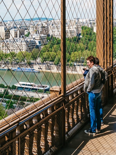 Visitors enjoying the view from the Eiffel Tower's second floor, overlooking the Seine River in Paris.