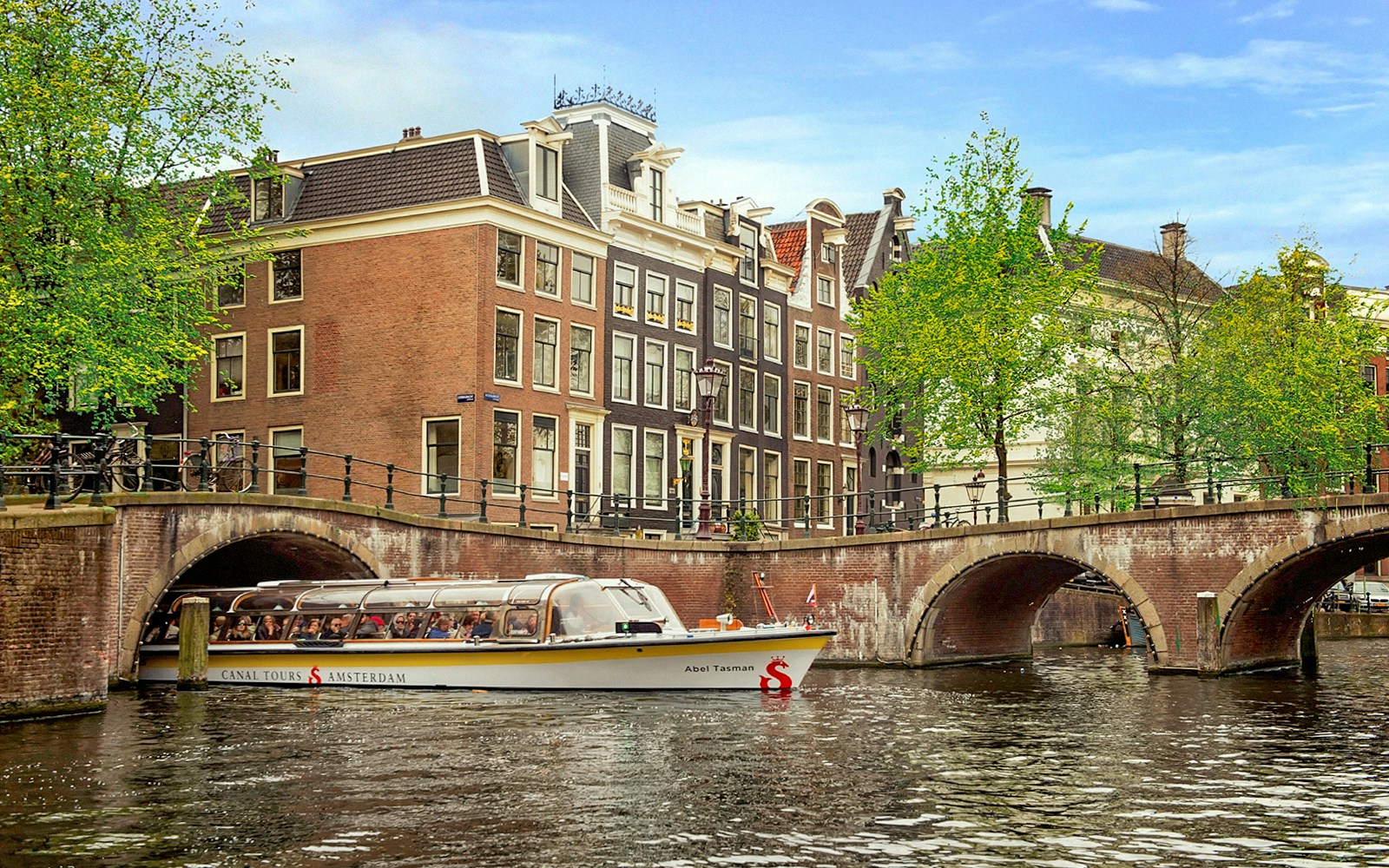 Amsterdam canal boat cruising past historic city center buildings.