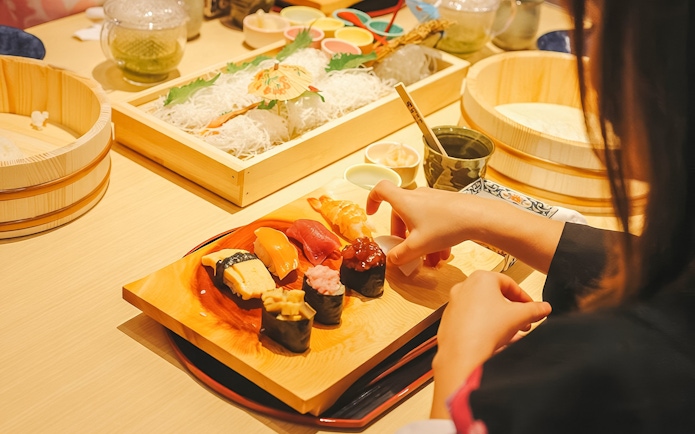 Tourist selecting sushi from a platter in a Japanese restaurant.