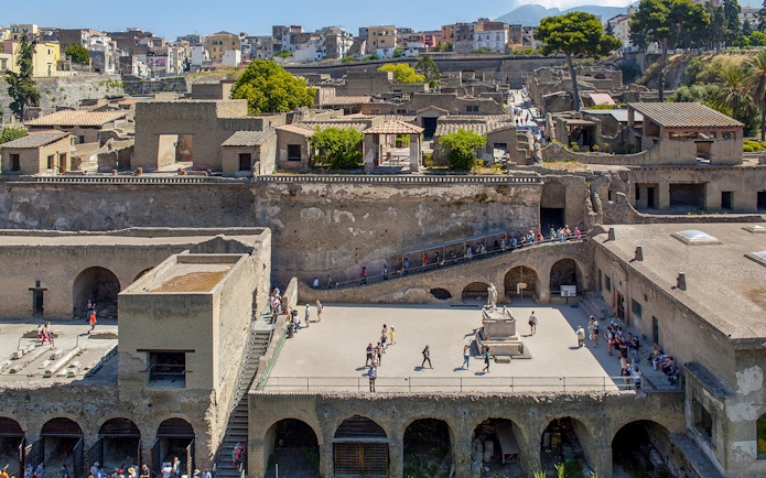 Visitors walking through the ancient ruins of Herculaneum basilica site.