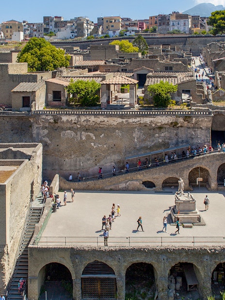 Visitors walking through the ancient ruins of Herculaneum basilica site.