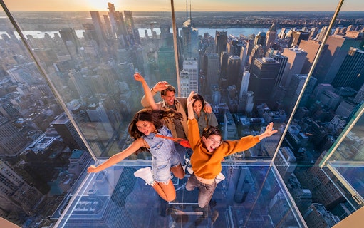 Group enjoying glass observation deck at SUMMIT One Vanderbilt, New York City skyline in background.