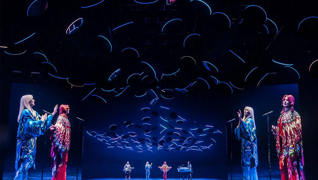 ABBA Voyage concert stage with holographic performers and dynamic lighting effects.
