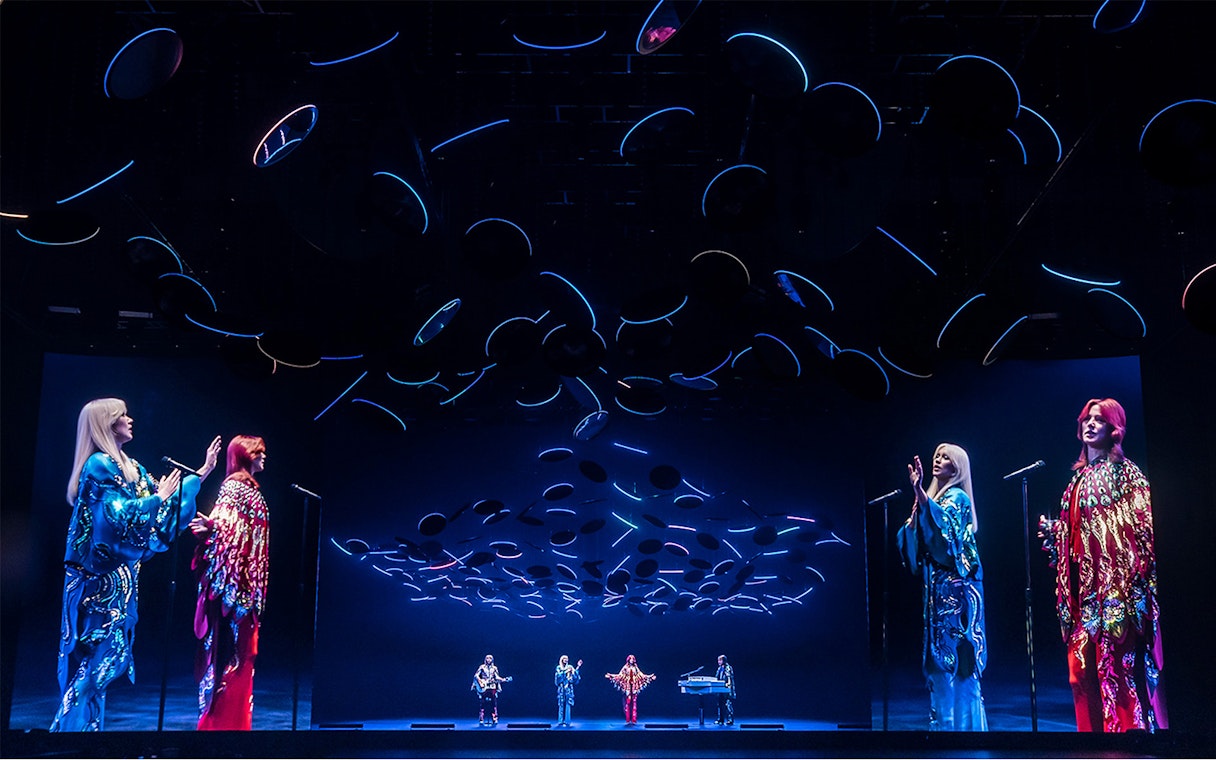 ABBA Voyage concert stage with holographic performers and dynamic lighting effects.