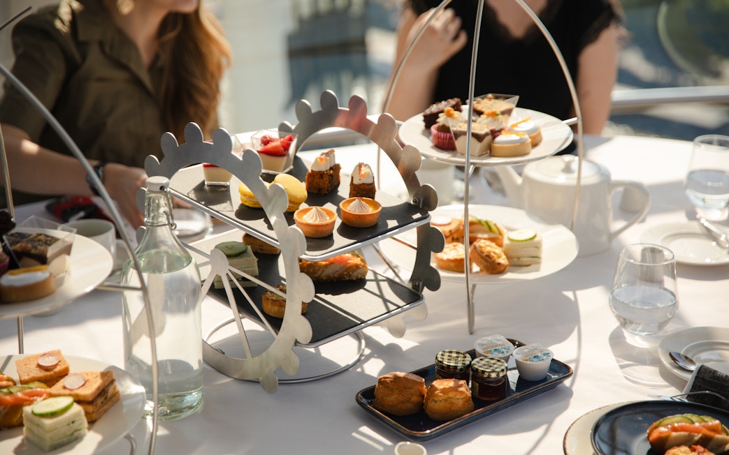 Afternoon tea setup with pastries and sandwiches on a London Eye-themed stand.
