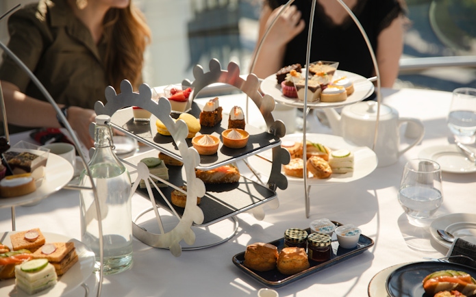 Afternoon tea setup with pastries and sandwiches on a London Eye-themed stand.