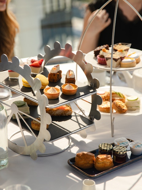Afternoon tea setup with pastries and sandwiches on a London Eye-themed stand.