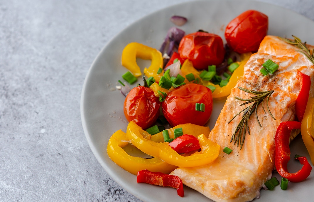 Arctic char fillet with cherry tomatoes and bell peppers on a plate.