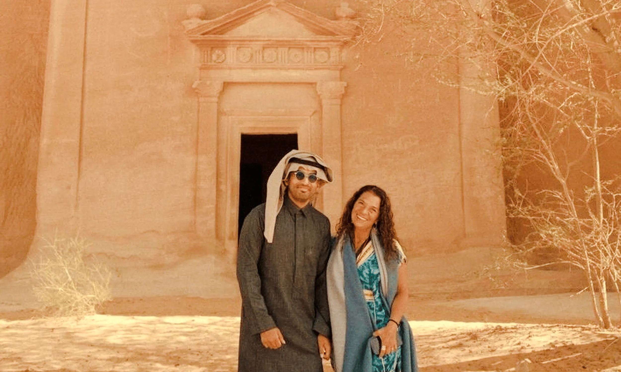 Couple standing in front of ancient Hegra tomb in AlUla, Saudi Arabia.