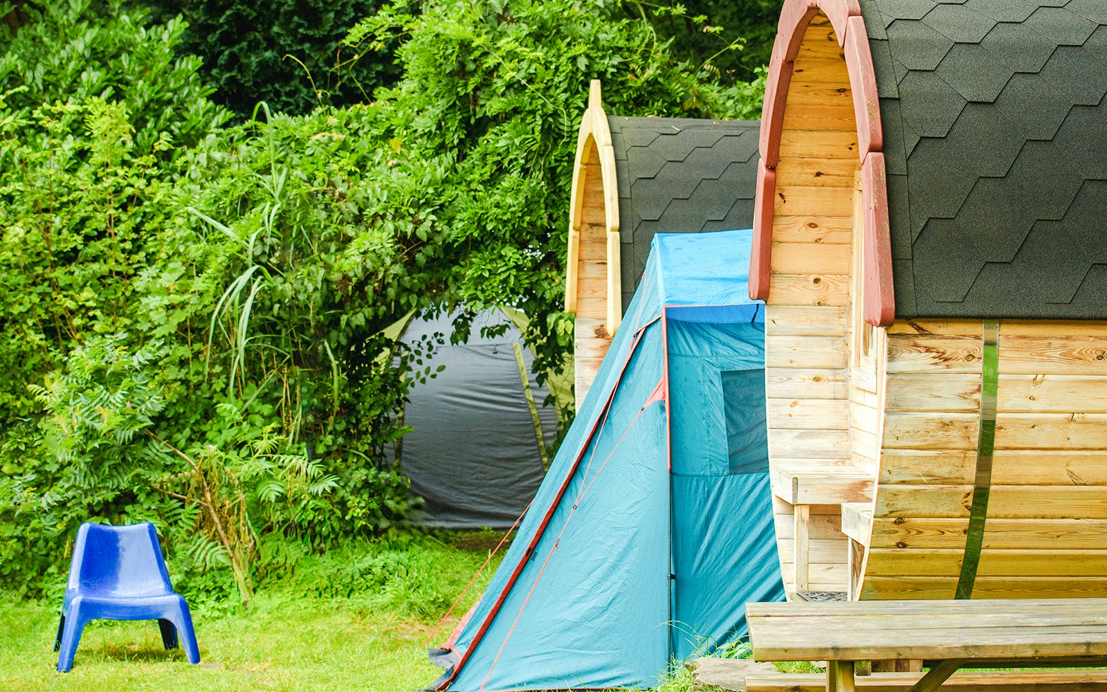 Barrel-shaped cabins and tent in lush Douro Valley setting.