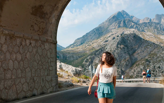 Mallorca mountain view with tourists walking under stone archway.