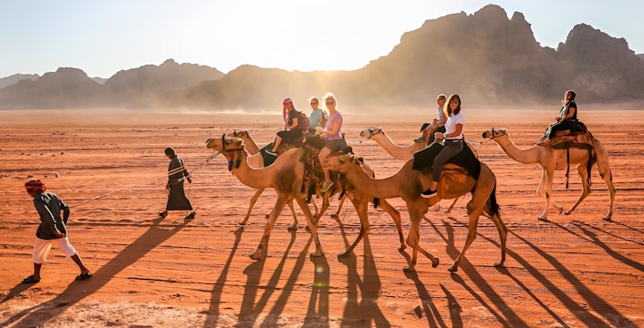 Camel ride in Palmeraie, Morocco at sunset with tourists and guides.