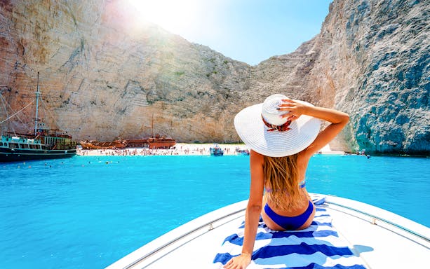 Speedboat approaching Shipwreck Island with tourists on deck, Navagio Beach, Greece.