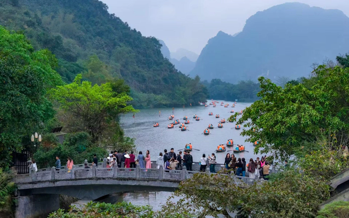 Visitors on a bridge overlooking boats on the river at Trang An Landscape Complex, Vietnam.