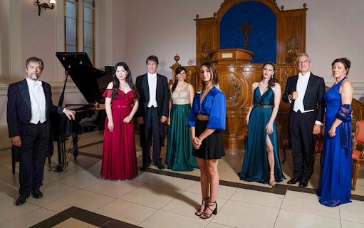 Opera performers in formal attire standing in a concert hall with a grand piano.