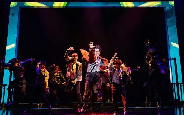 Performers energetically dancing on stage during The Who’s Tommy musical.