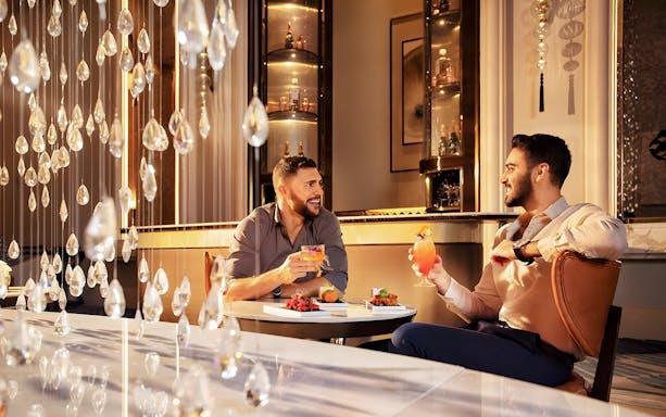 Men enjoying signature cocktails with cake at Pearl Afternoon Tea, Platos.