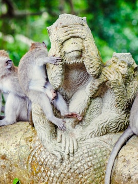 Monkeys interacting with a stone statue in Sacred Monkey Forest, Bali.