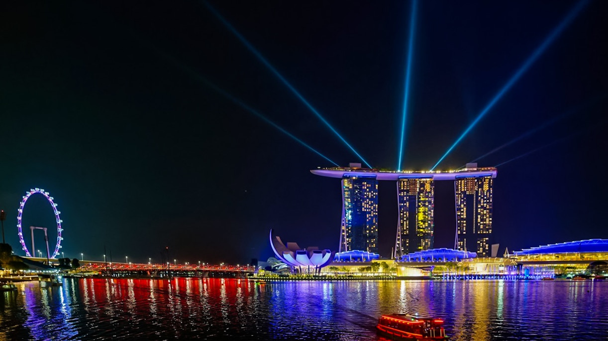 Marina Bay Sands illuminated at night with light beams, Singapore Flyer in the background.