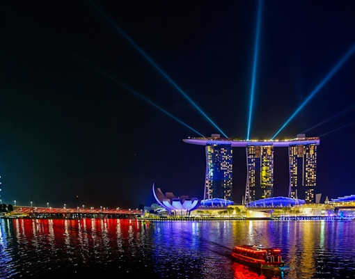 Marina Bay Sands illuminated at night with light beams, Singapore Flyer in the background.