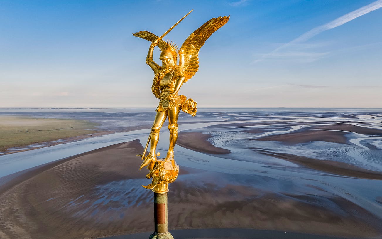 Golden statue of Saint Michael atop Mont Saint Michel Abbey with tidal flats in Normandy, France.