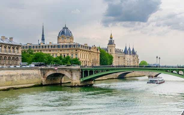 Seine River cruise boat passing under a bridge near historic Paris buildings.