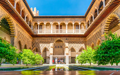 Tour group exploring Alcazar of Seville's Moorish architecture courtyard.